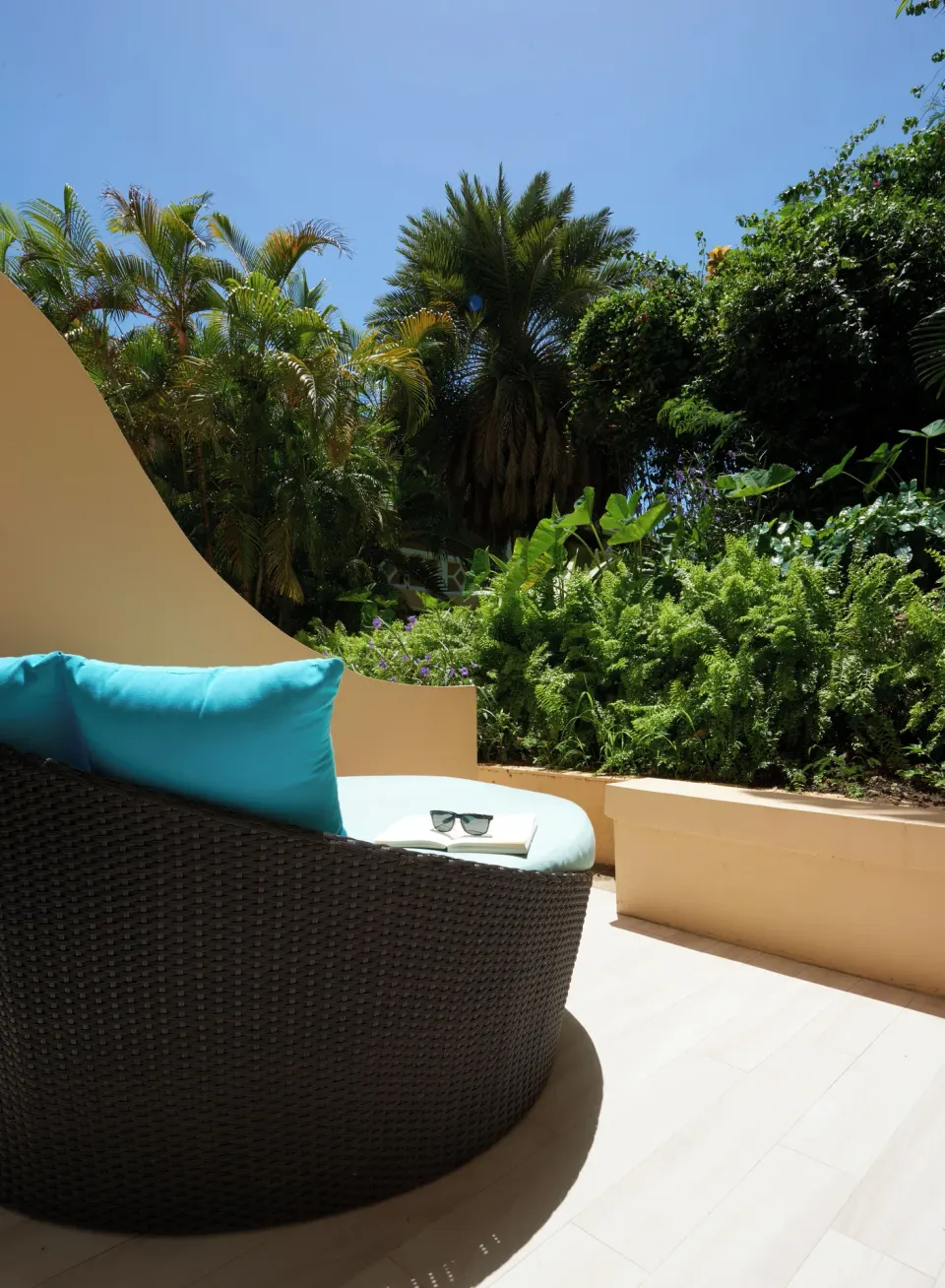 BodyHoliday terrace with a curved wicker lounger, blue cushions, and dense tropical planting.