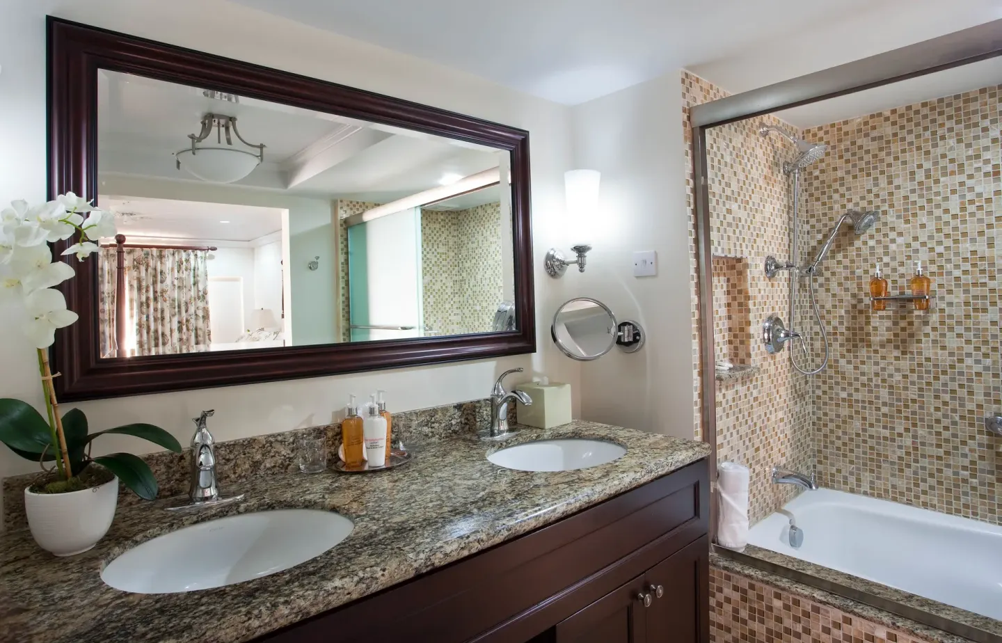 BodyHoliday bathroom with double sinks, granite counter, large mirror, and tiled tub-shower.