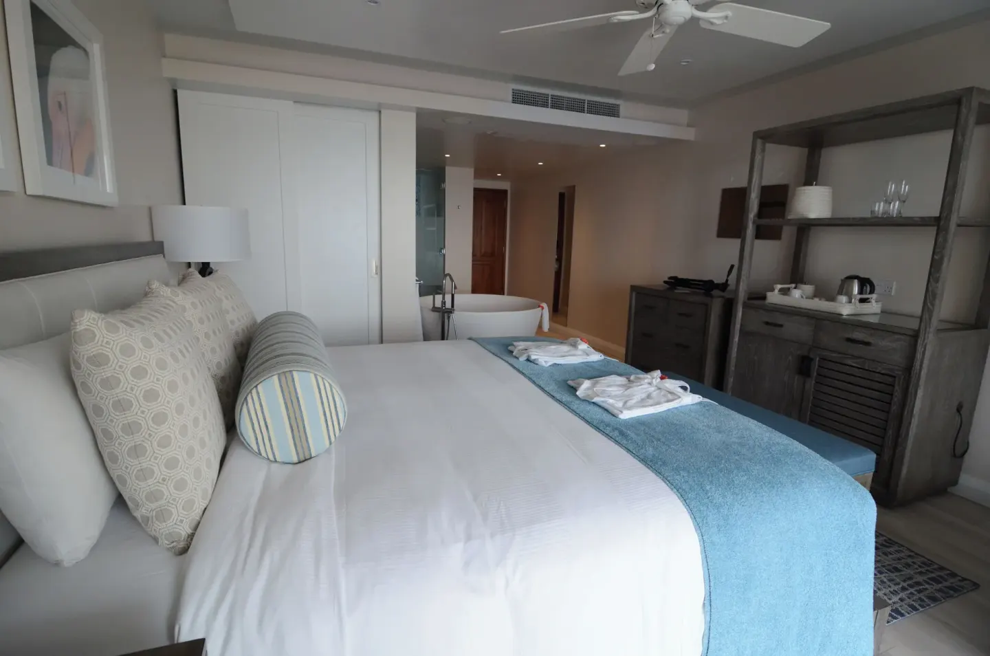 King-bed suite at BodyHoliday with open bathtub, ceiling fan and refreshment cabinet.