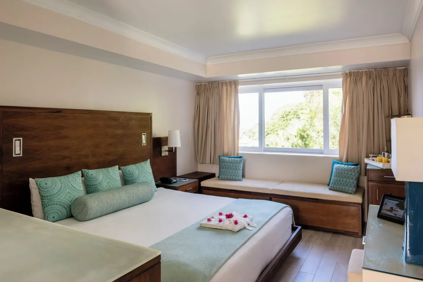 King-bed guest room at BodyHoliday with window bench, aqua pillows and refreshment area.