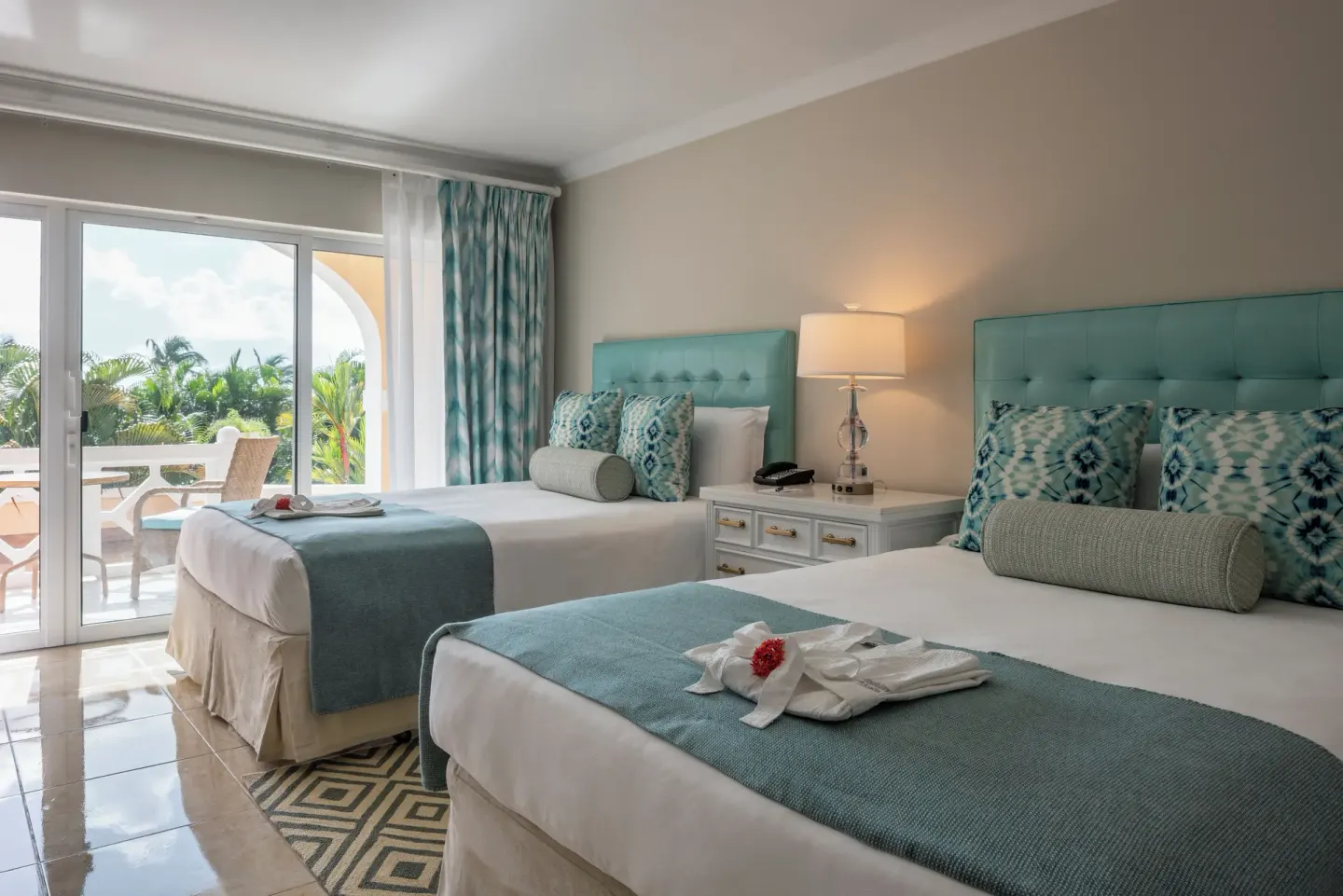 Two double beds at BodyHoliday with aqua headboards and balcony beside tropical greenery.