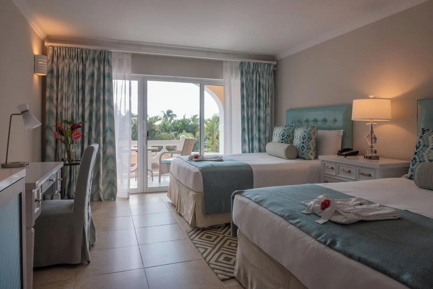 Double-bed guest room at BodyHoliday with desk and balcony doors facing palms.