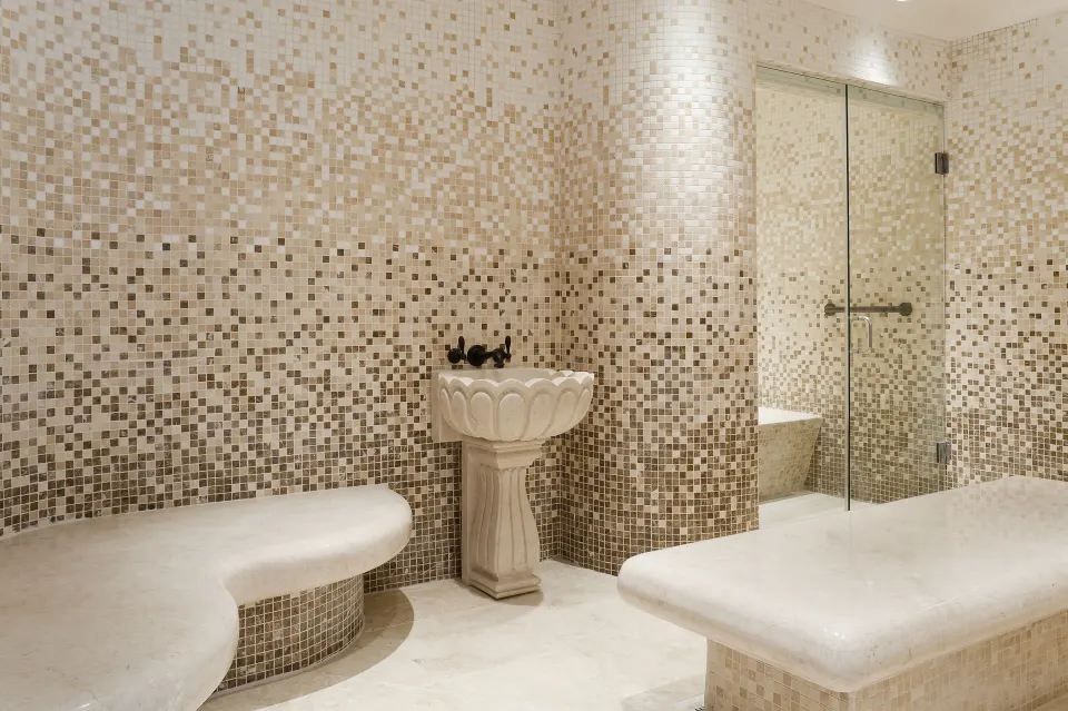 Mosaic-tiled spa room with benches, basin, and glass shower at BodyHoliday.