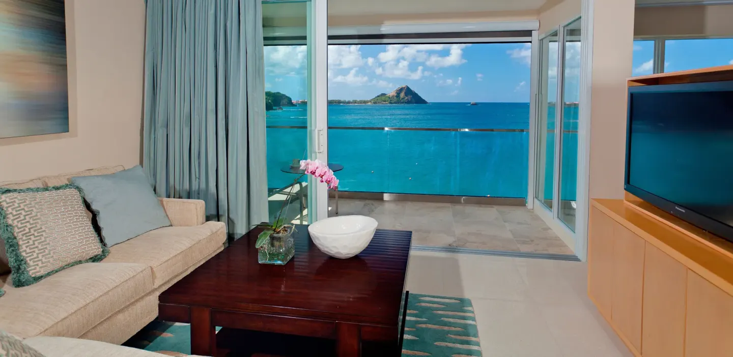 Suite lounge with sofa, television, and open balcony facing the sea at BodyHoliday.