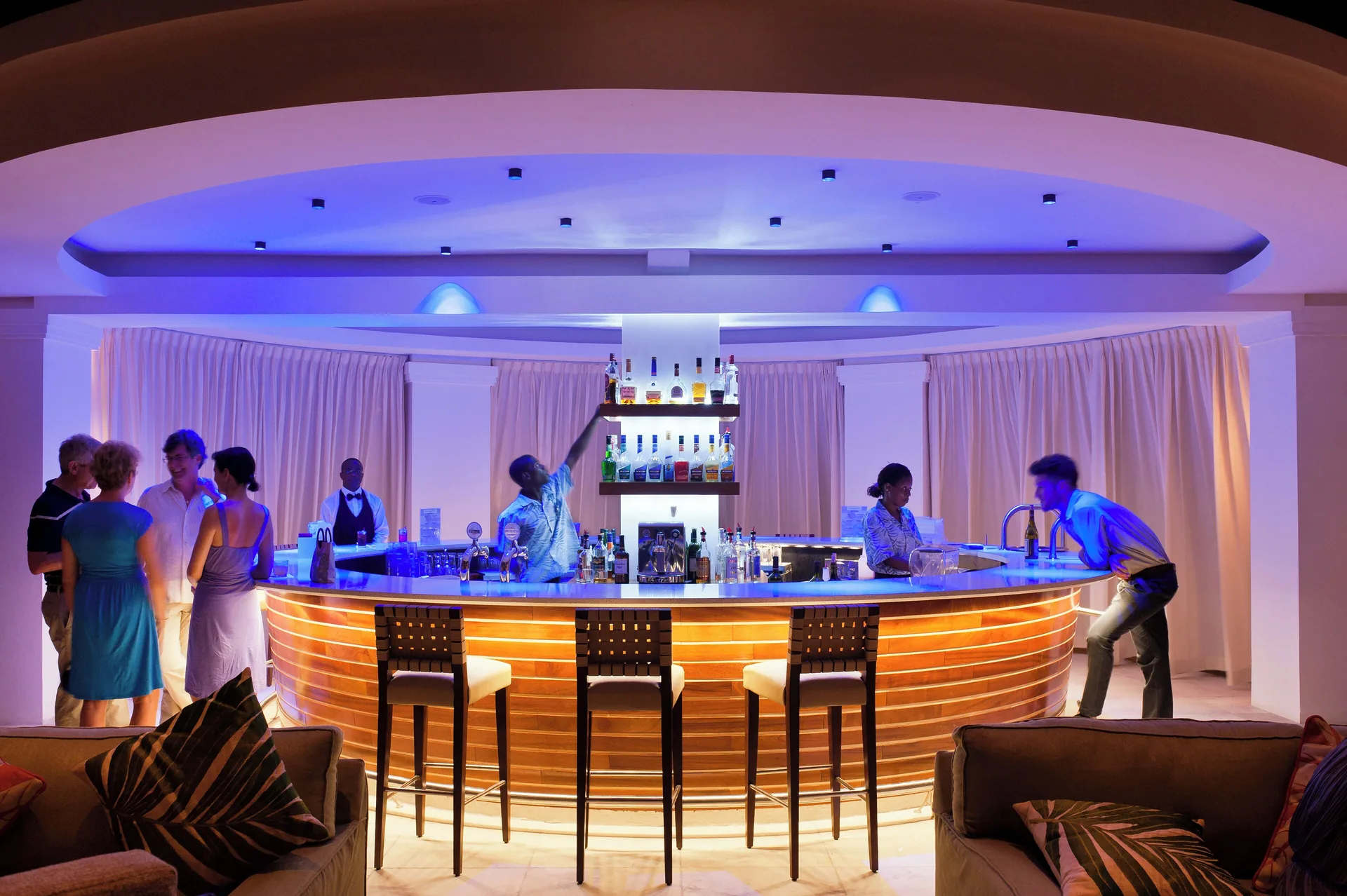 Guests sit at a blue-lit bar with bartenders serving drinks at BodyHoliday.