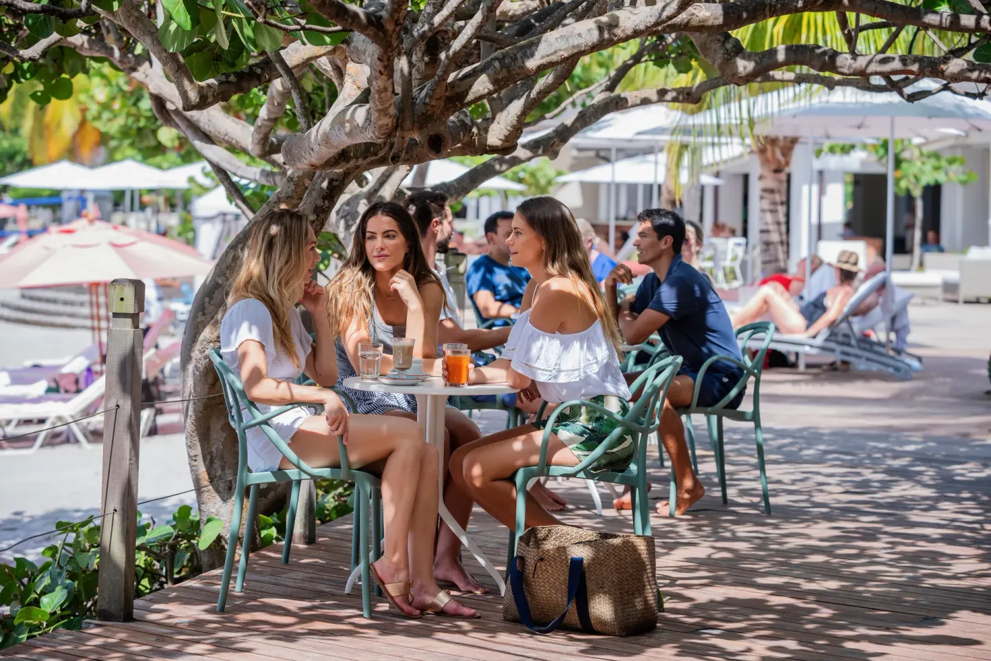 Guests sit with drinks at a shaded poolside cafe table at BodyHoliday.