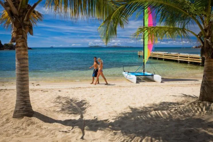 Couple walks past a small sailboat on the beach at Bolongo Bay Beach Resort.