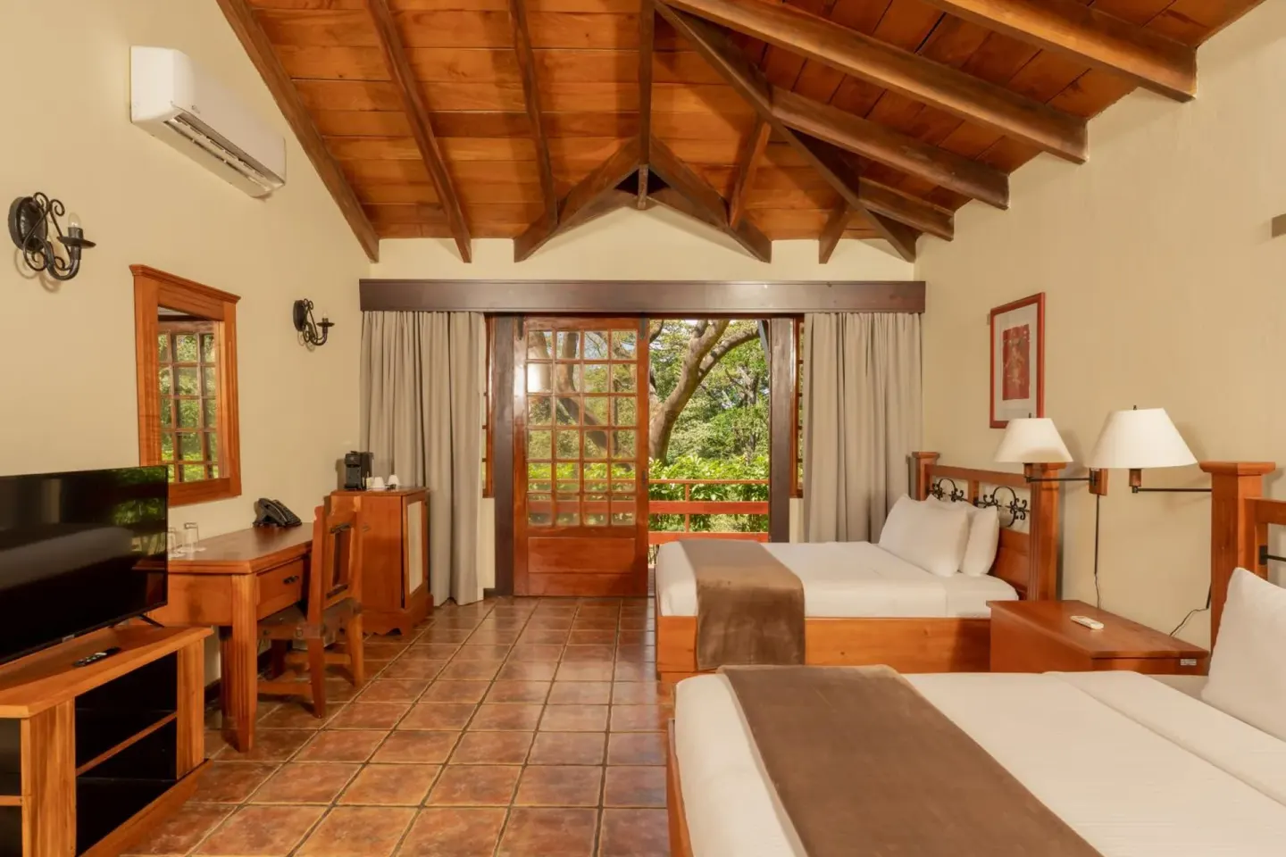 Guest room with two beds, wood ceiling, balcony doors, and TV at Borinquen Thermal Resort.