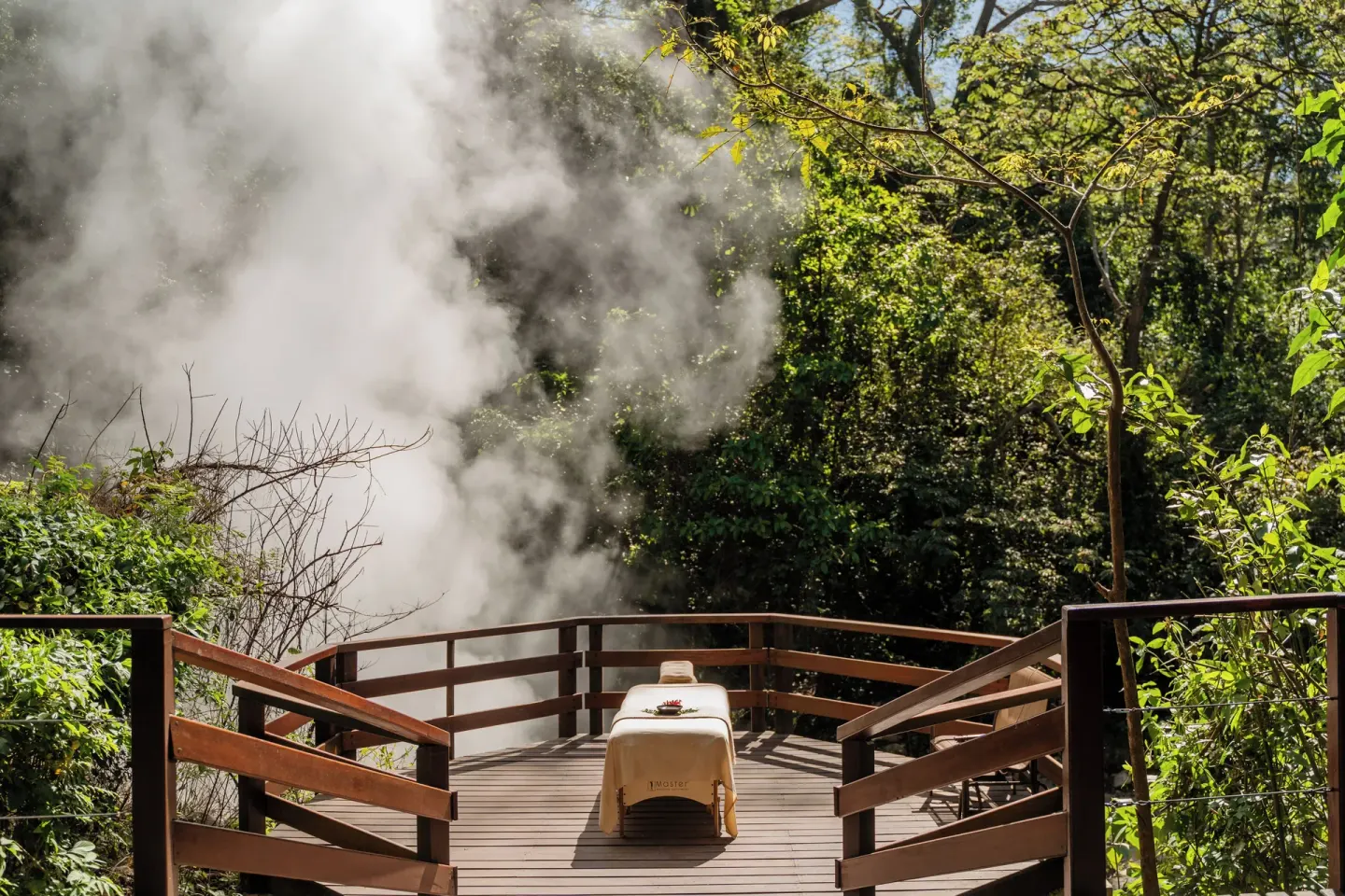 Massage table on a wooden deck beside steam at Borinquen Thermal Resort.