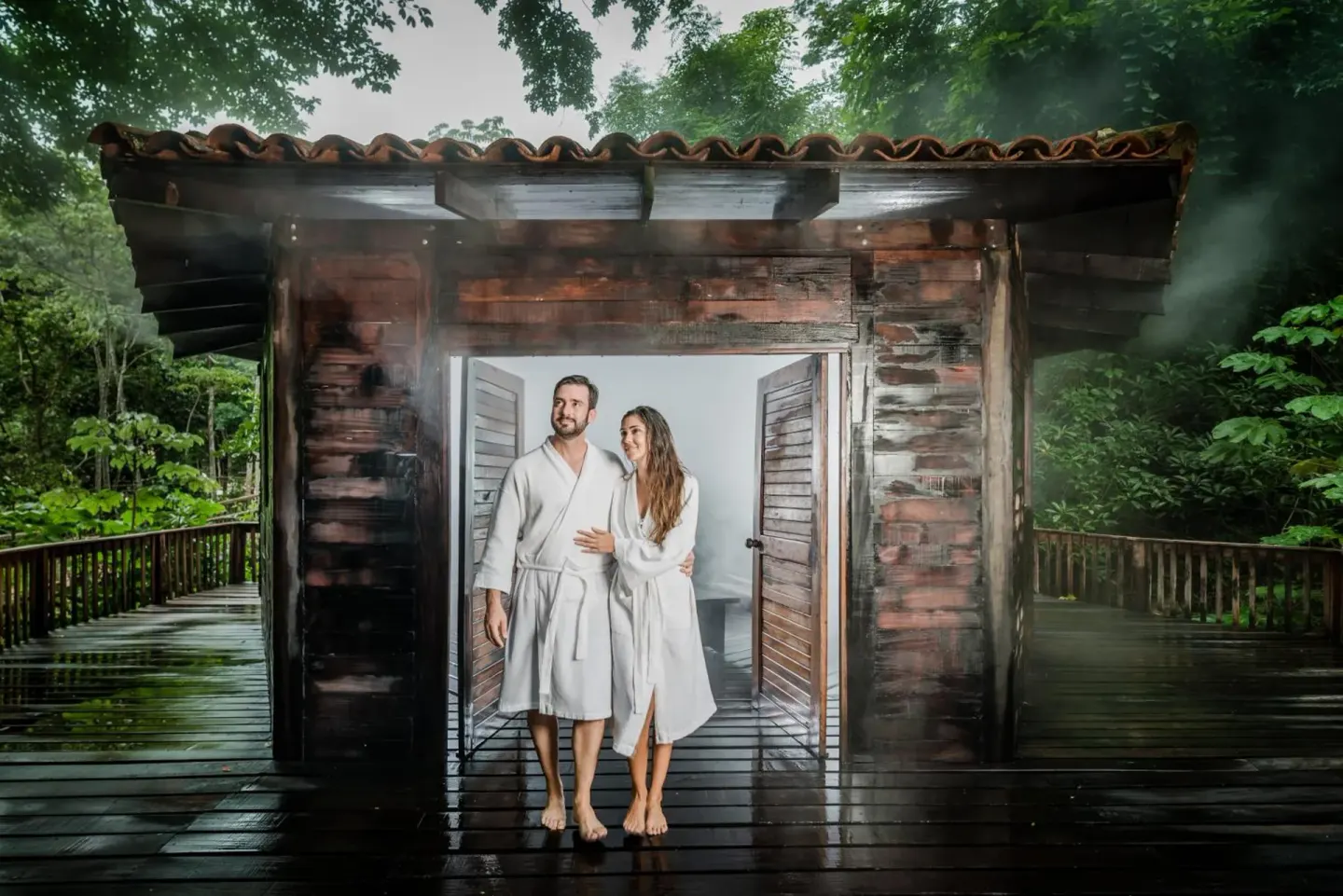 Couple in robes standing in a steamy wooden spa building at Borinquen Thermal Resort.
