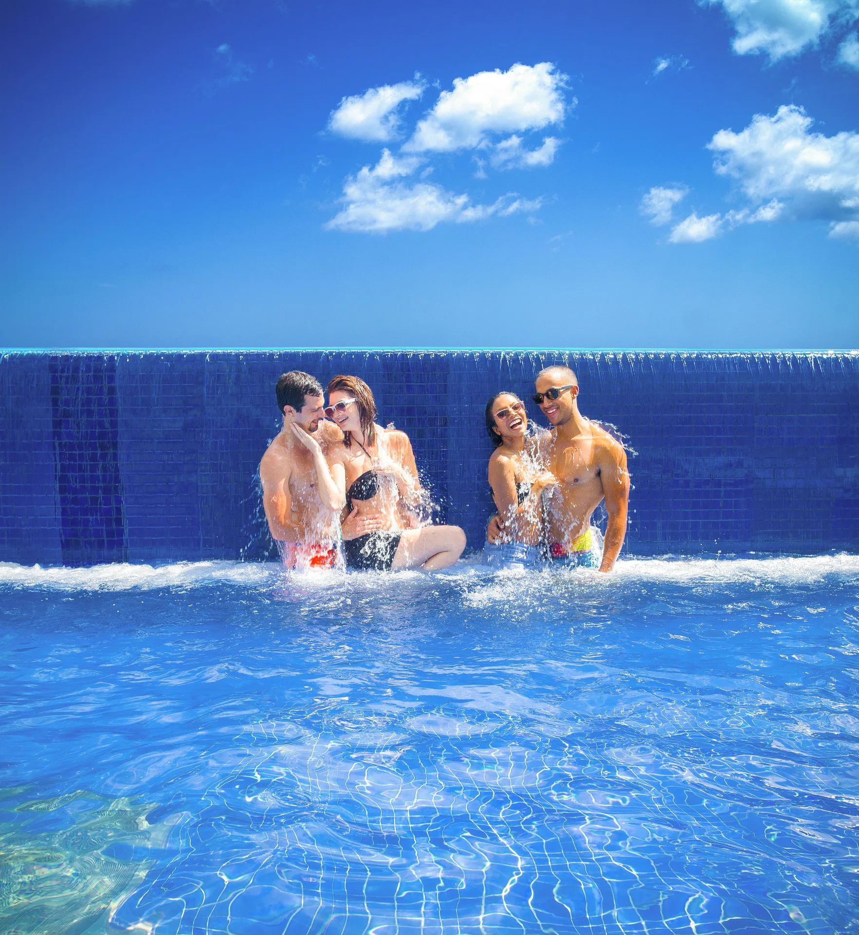 Guests sitting in a blue pool beneath a waterfall edge at Breezes Resort Bahamas.