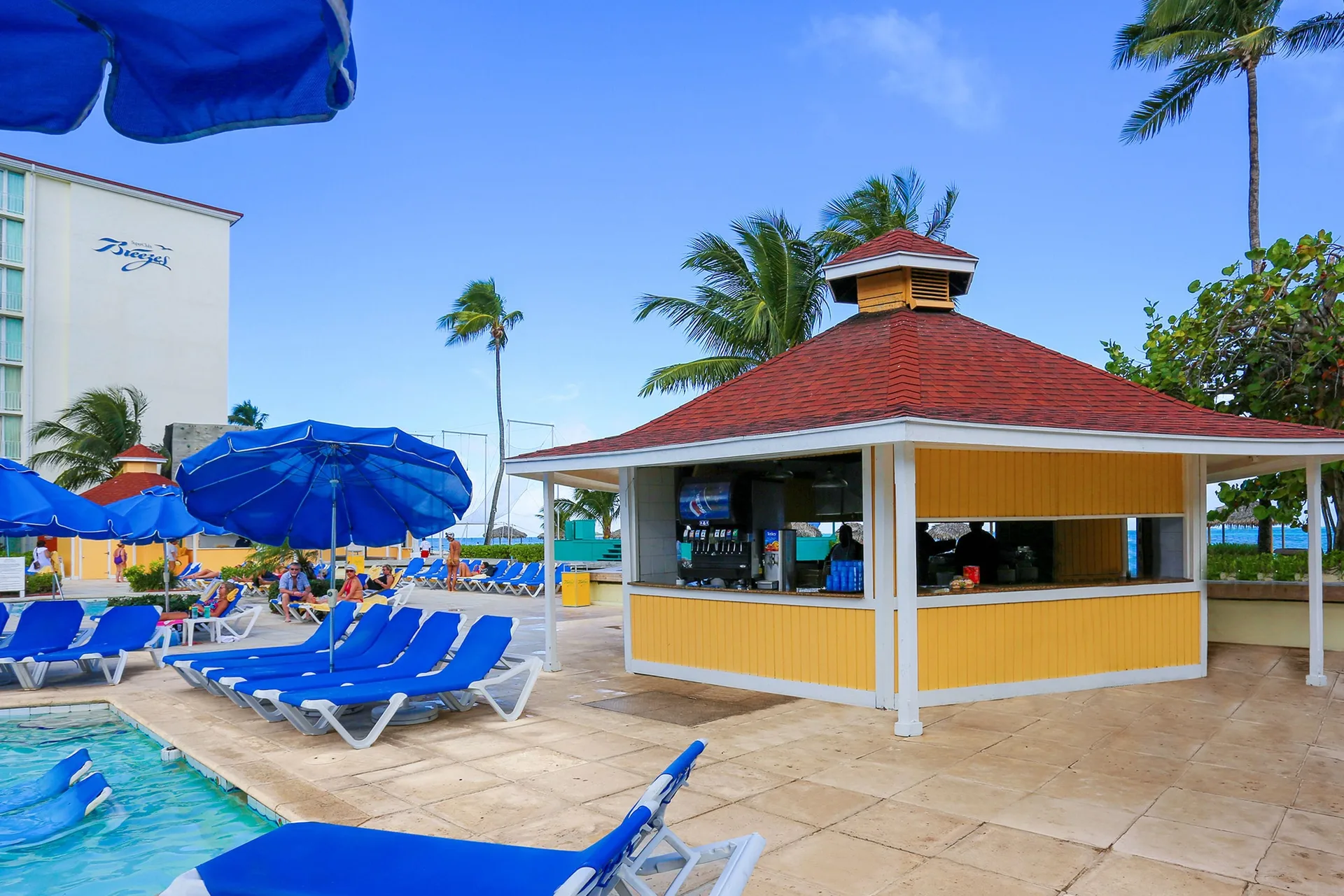 Poolside snack bar, blue loungers, and umbrellas at Breezes Resort Bahamas.