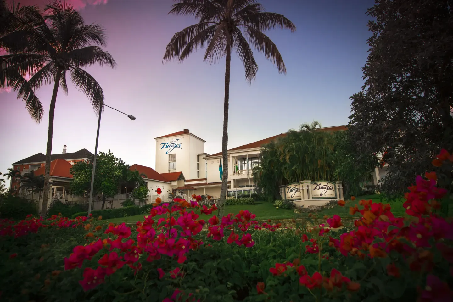 Resort entrance, palm trees and flowers at dusk at Breezes Resort Bahamas.