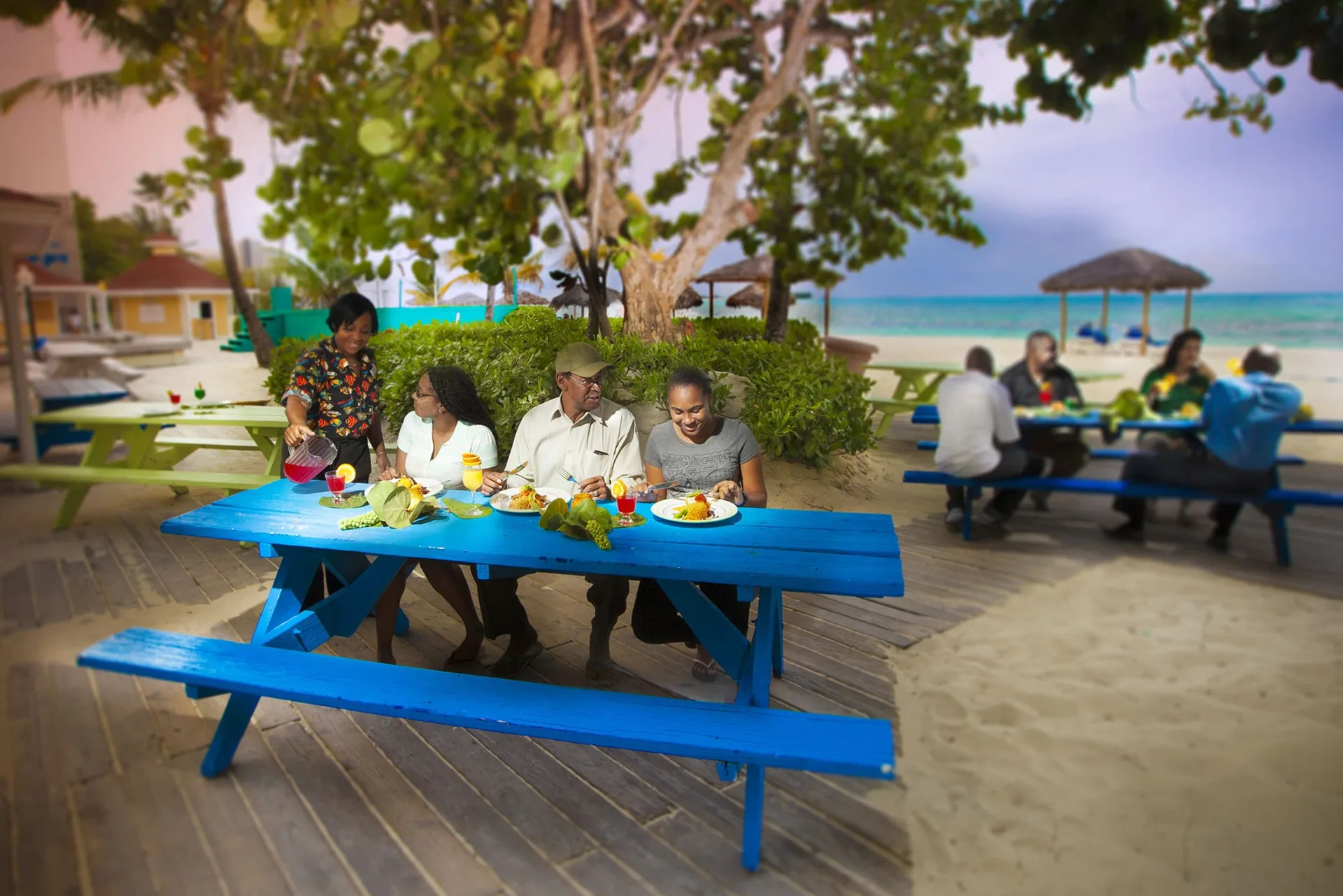 Guests dining at blue picnic tables near the beach at Breezes Resort Bahamas.