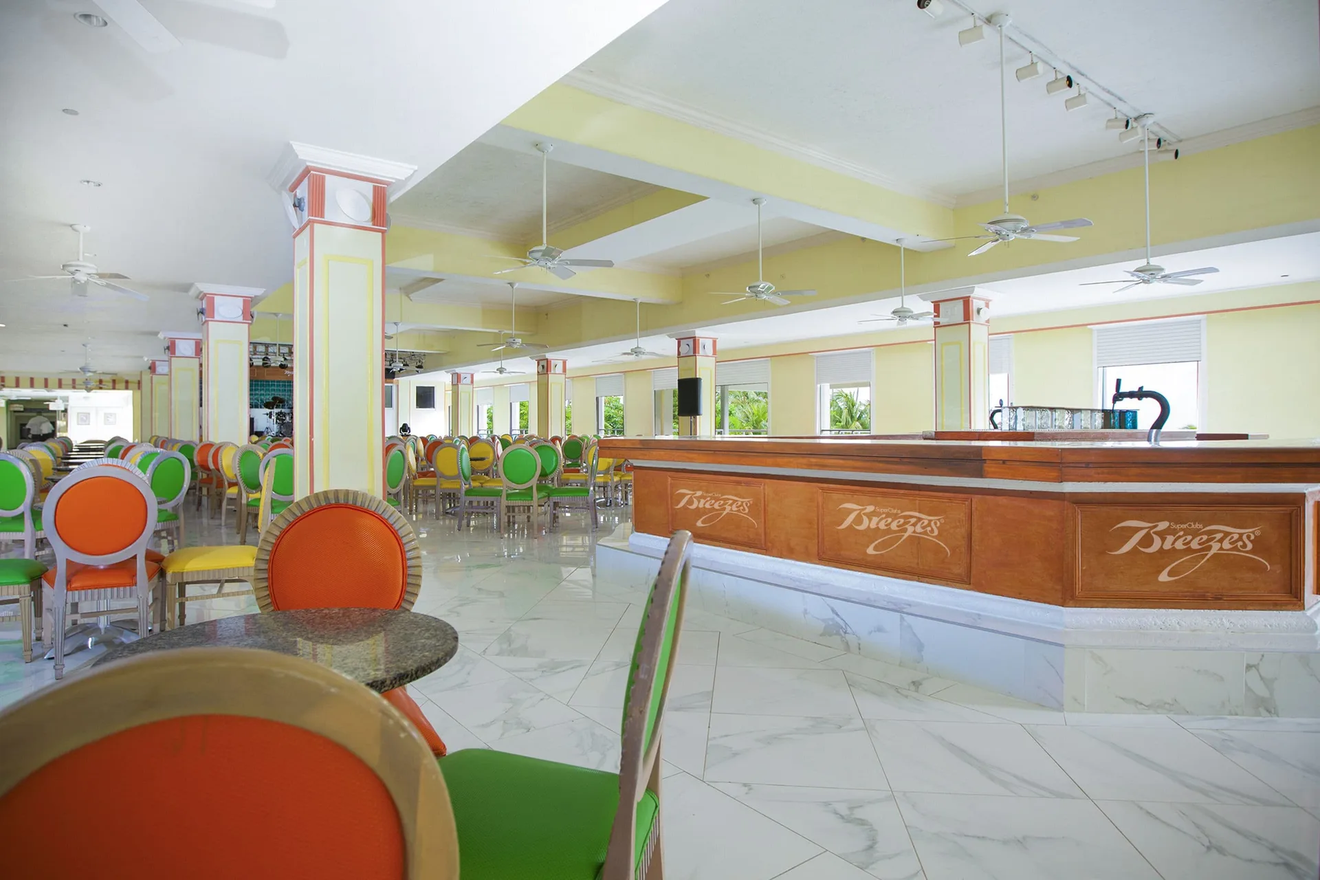 Open dining room with bright chairs and a wood service counter at Breezes Resort Bahamas.