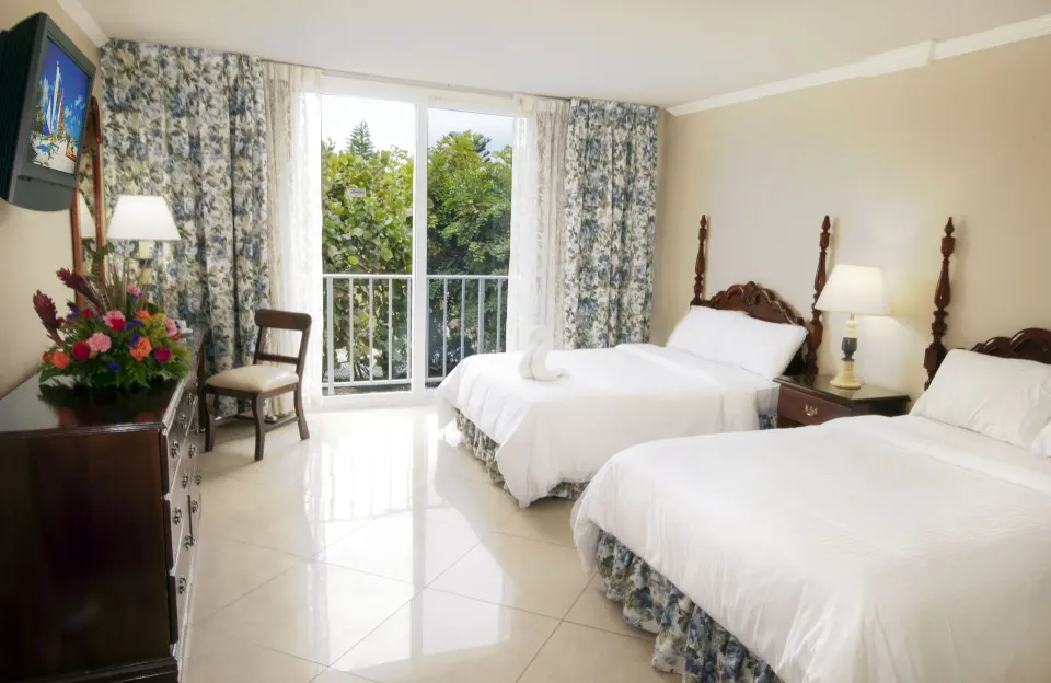 Classic Room with two beds, balcony doors, and garden views at Breezes Resort Bahamas.