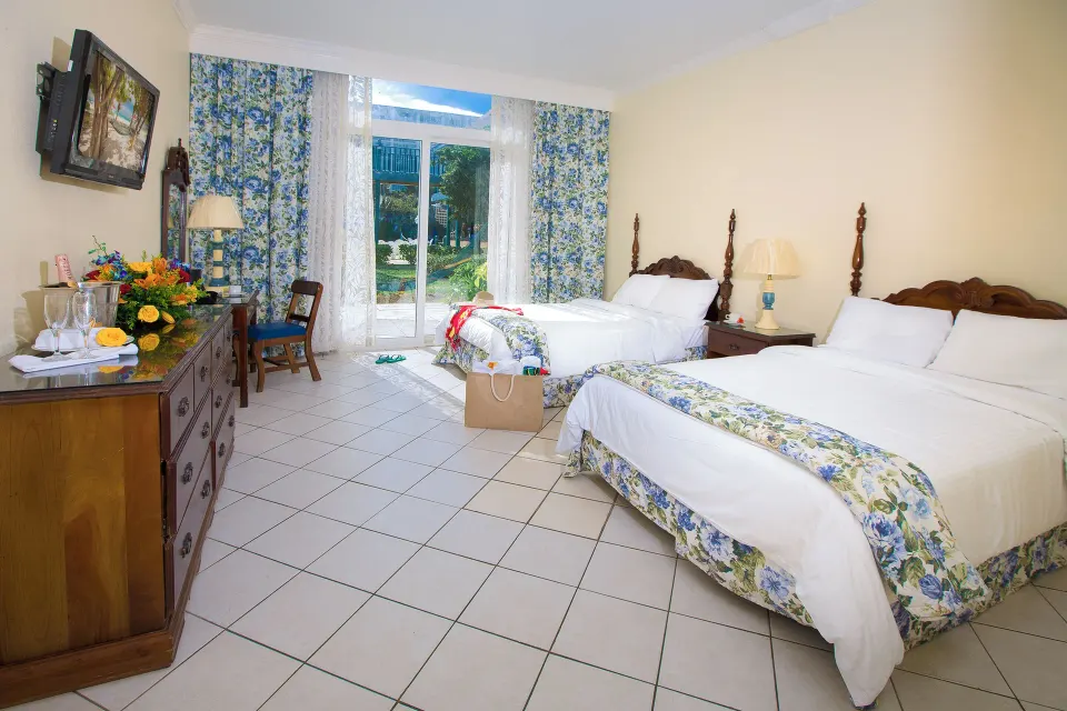 Patio Room with two beds, dresser, TV, and garden-facing doors at Breezes Resort Bahamas.