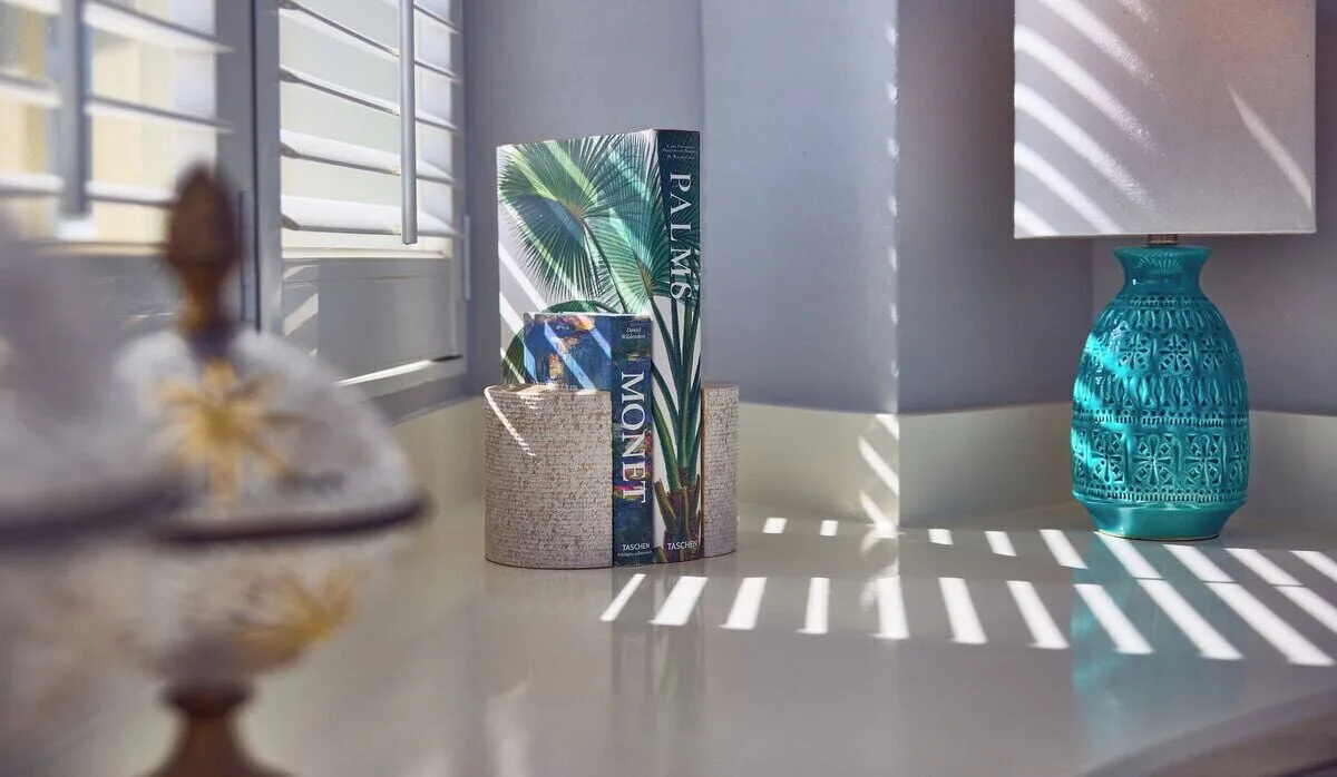 Guest room desktop with shutters, turquoise lamp, books, and striped sunlight at British Colonial Nassau.