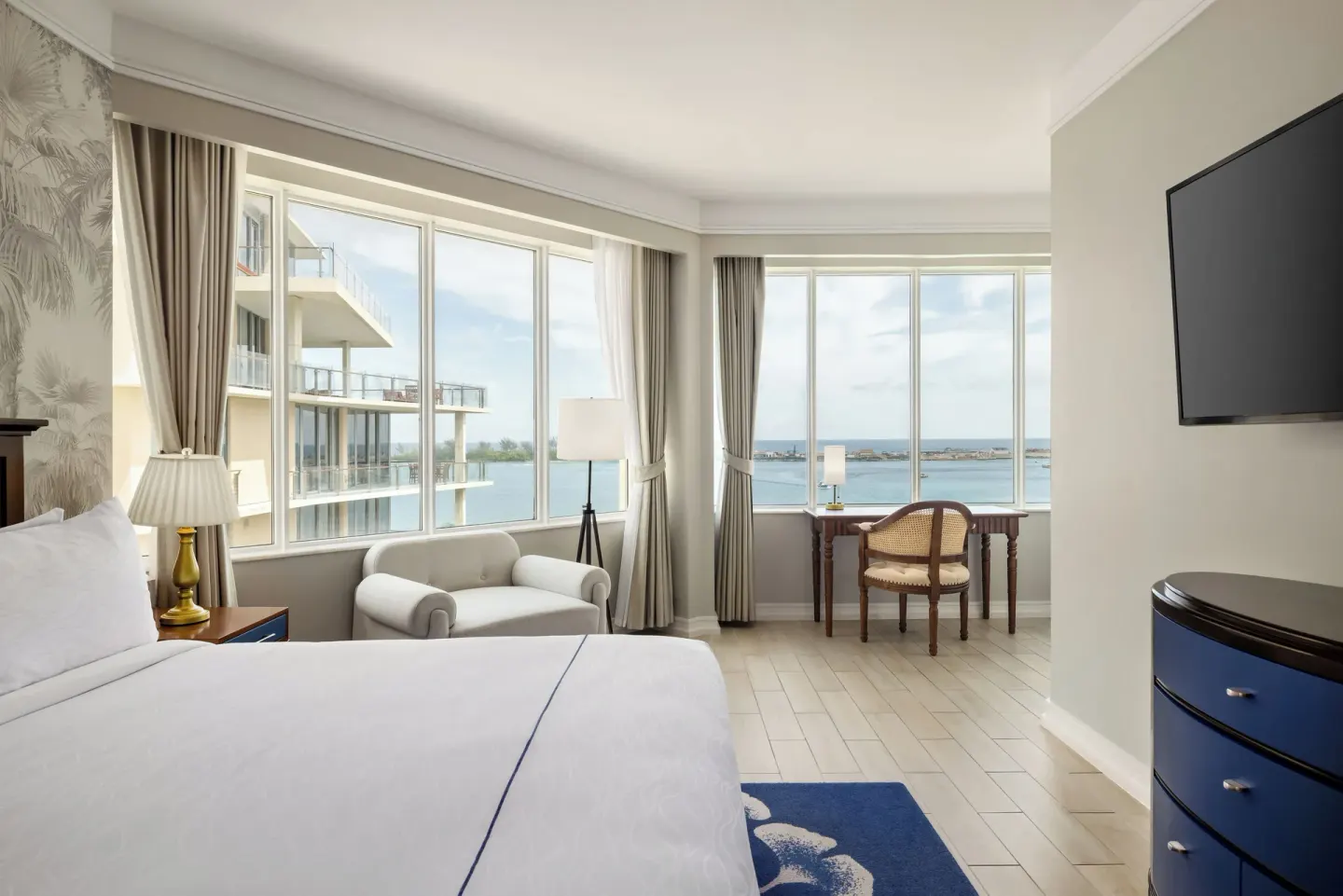 Guest room with a king bed, seating, desk, TV, and harbor-facing windows at British Colonial Nassau.