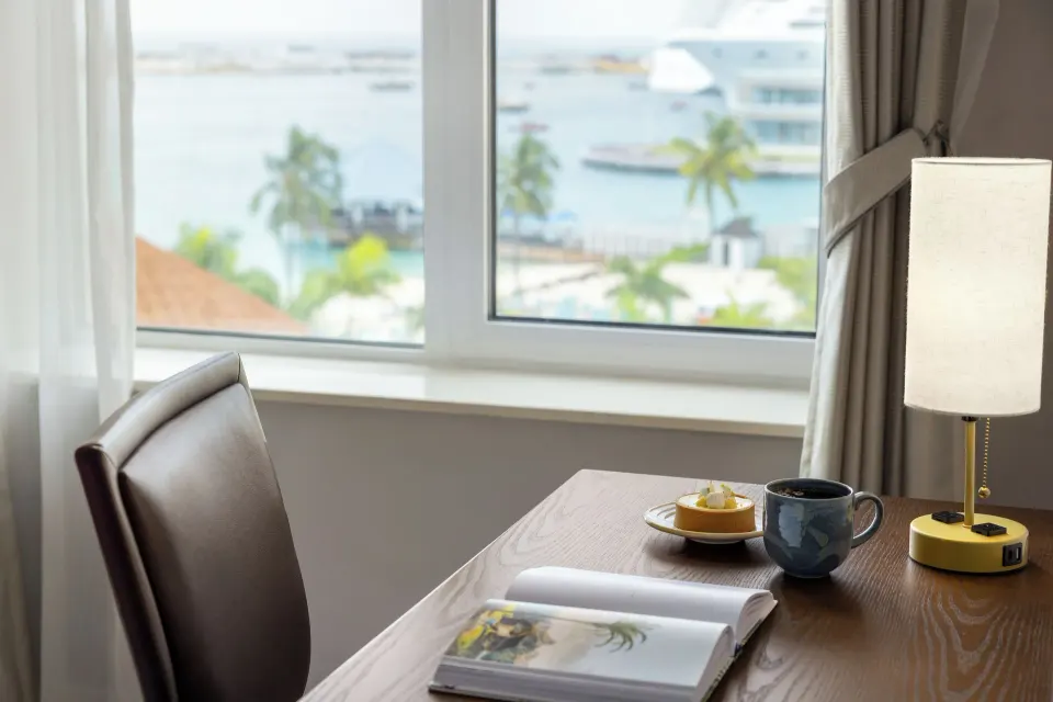 Ocean View room desk with lamp, mug, open book, and harbor view at British Colonial Nassau.