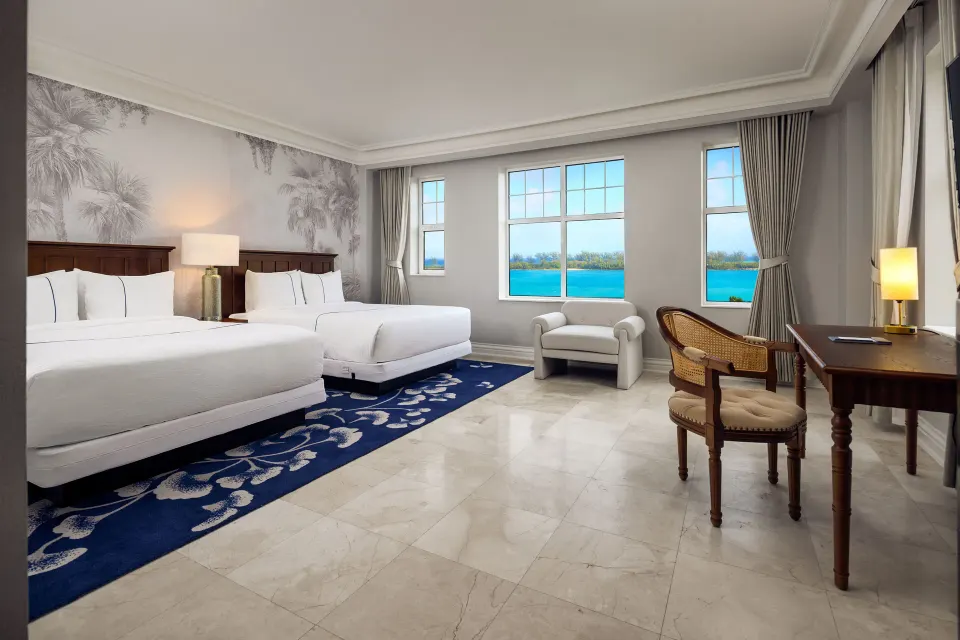 Ocean View room with two beds, desk, armchair, and blue water views at British Colonial Nassau.