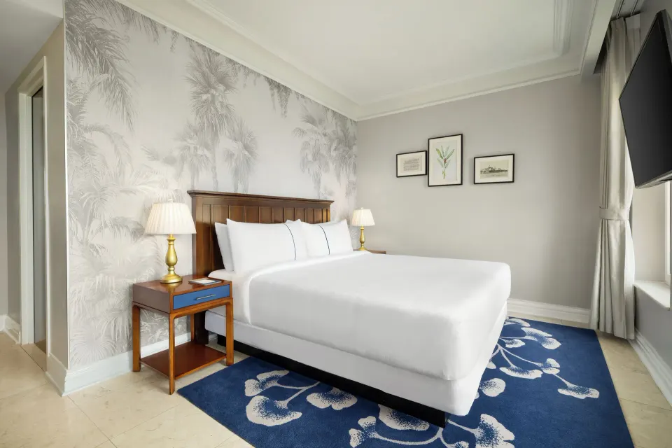 Standard Room king bed with palm wallpaper and blue rug at British Colonial Nassau.