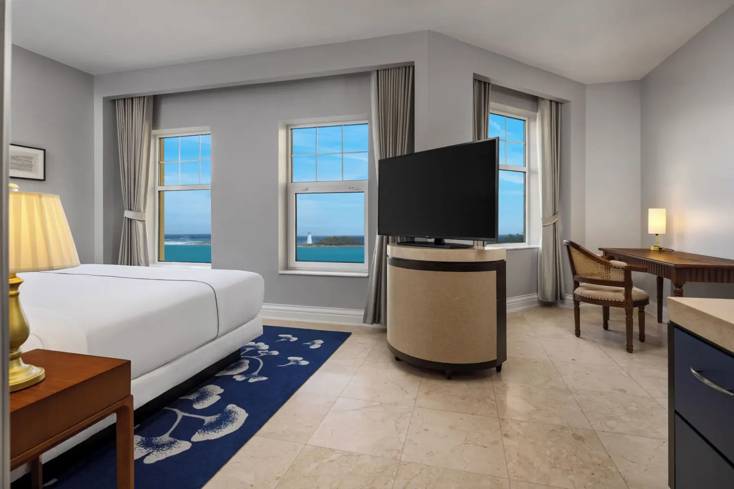 Standard Suite bedroom with king bed, TV, desk, and harbor-view windows at British Colonial Nassau.