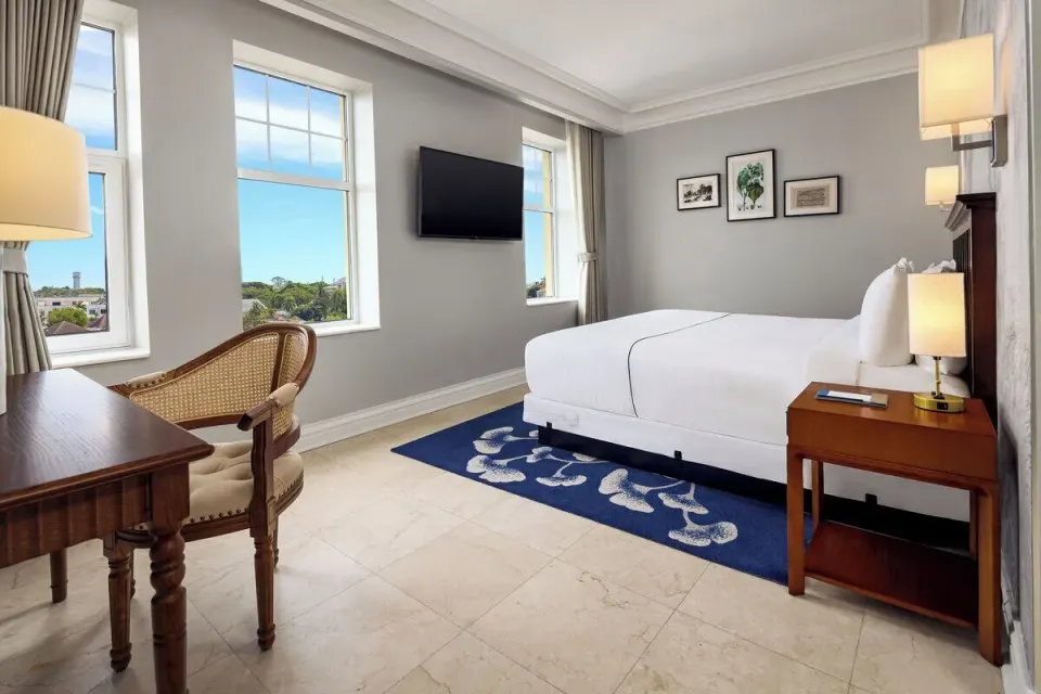 City View Suite bedroom with a white bed, desk, and tall windows at British Colonial Nassau.