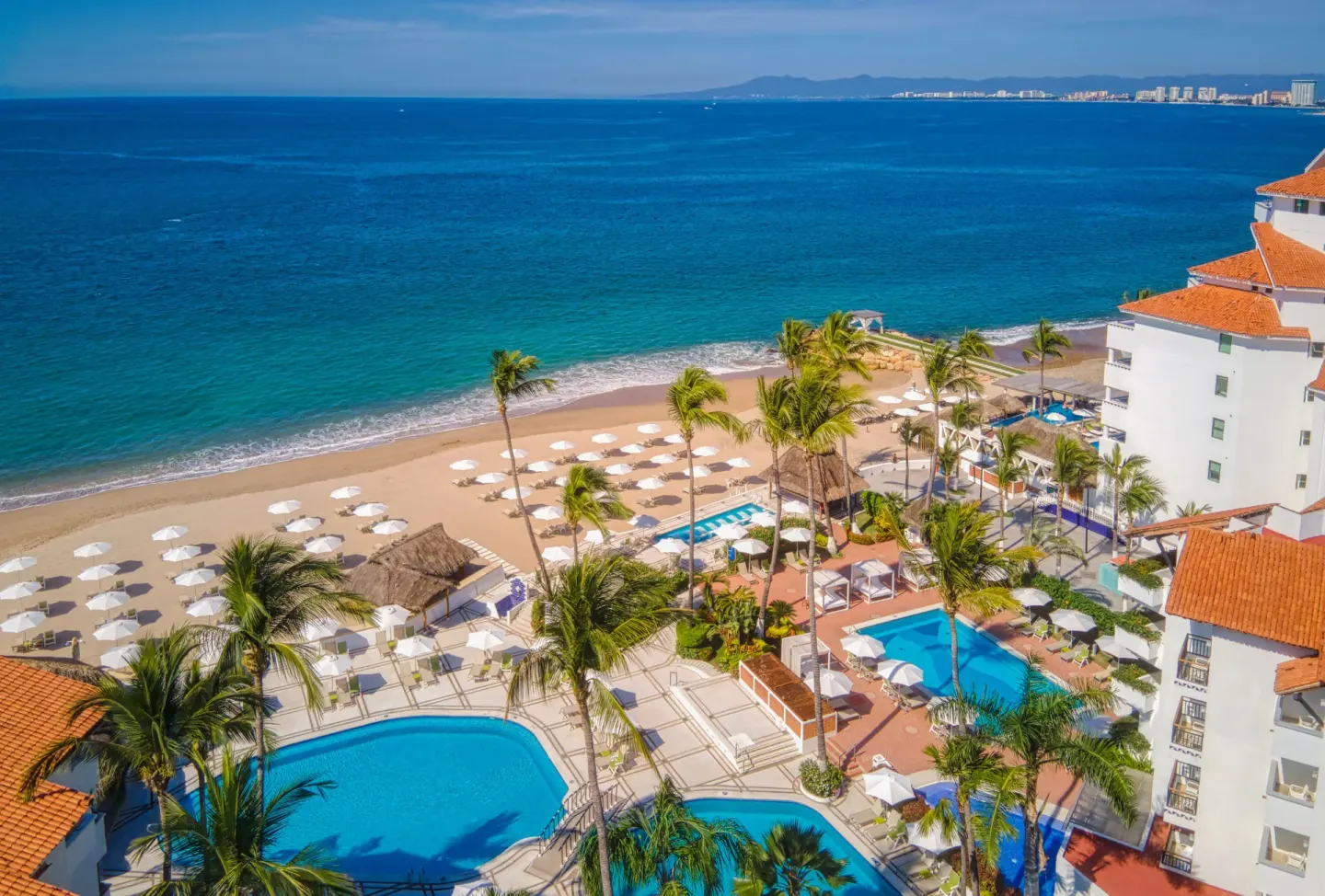 High resort view at Buenaventura Grand Hotel & Great Moments showing pools, beach umbrellas, and blue ocean.
