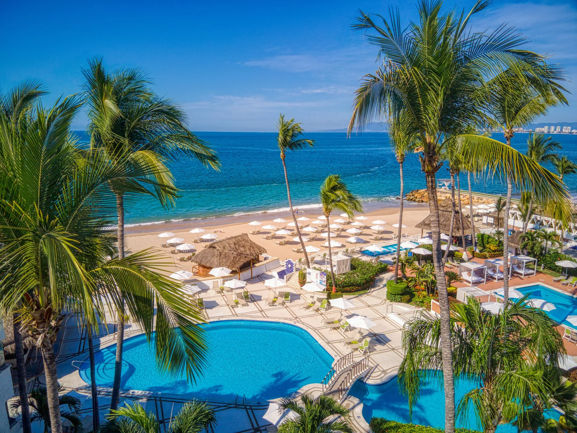 Palm-framed pool and beach at Buenaventura Grand Hotel & Great Moments beside the blue ocean.