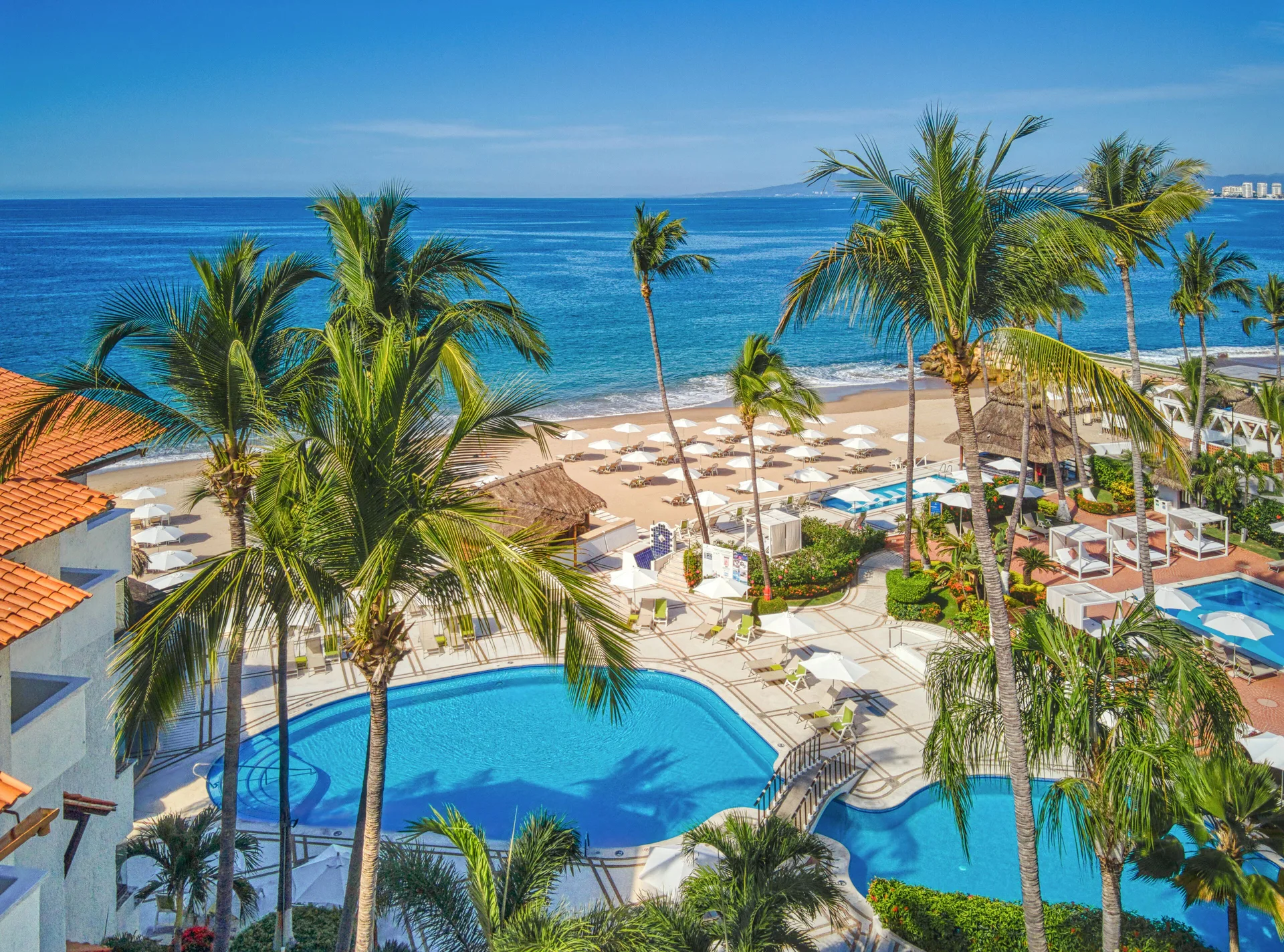 Resort pools and beach at Buenaventura Grand Hotel & Great Moments seen through tall palm trees.