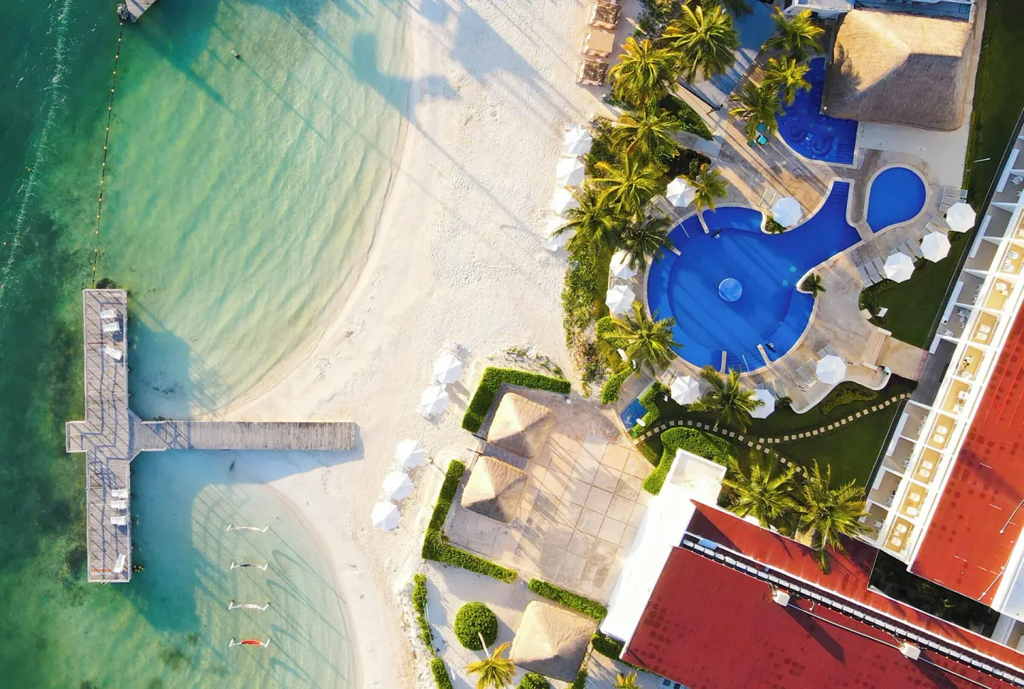 Aerial view of the beach, pier, pools, palms, and resort buildings at Cancun Bay Hotel.