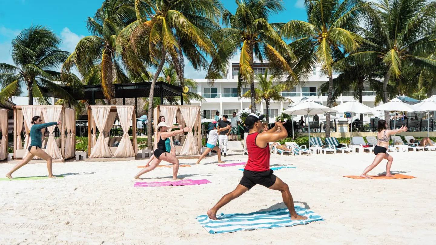 Guests exercise on beach towels beneath palm trees at Cancun Bay Hotel.