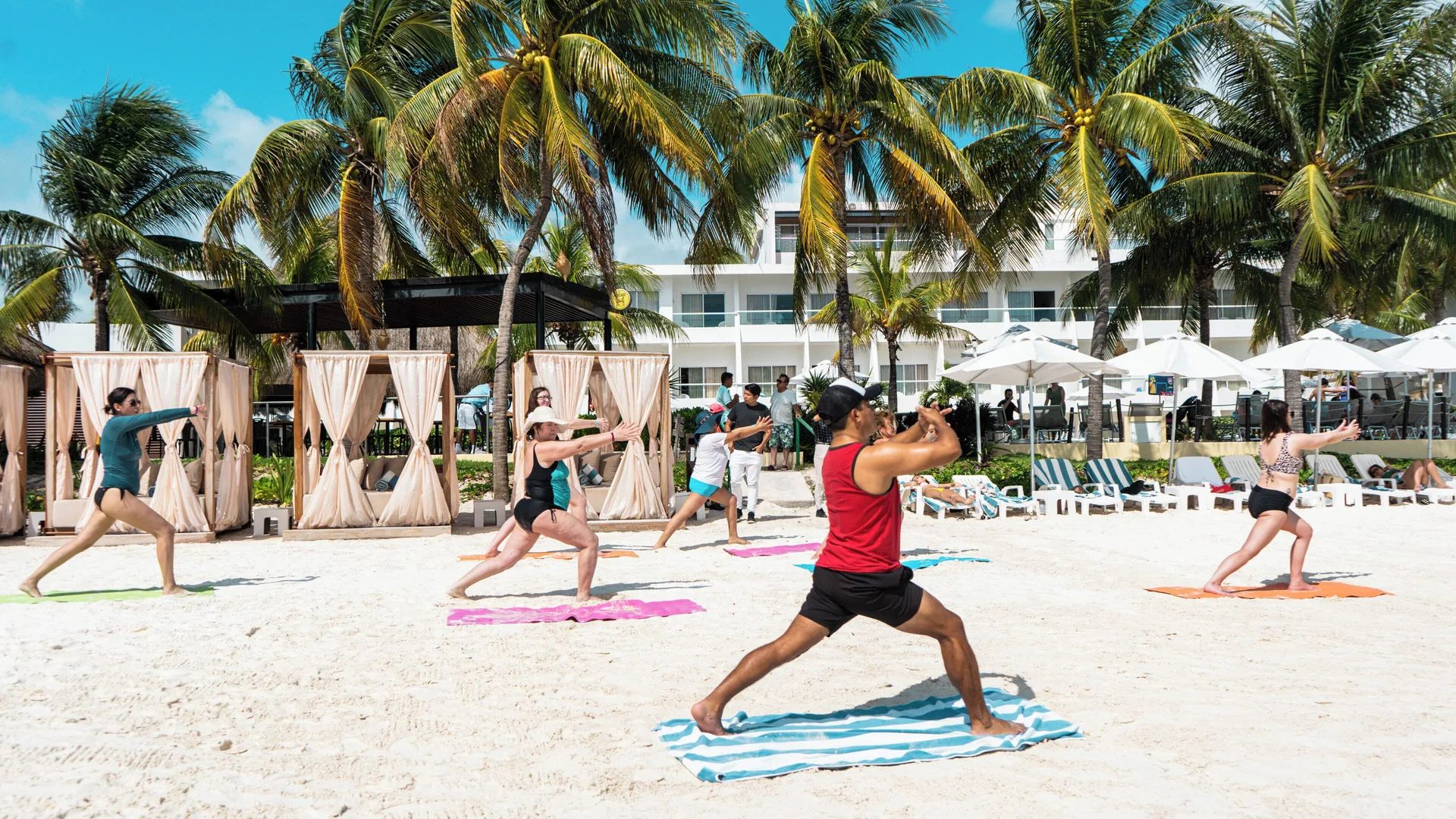 Guests exercise on beach towels beneath palm trees at Cancun Bay Hotel.