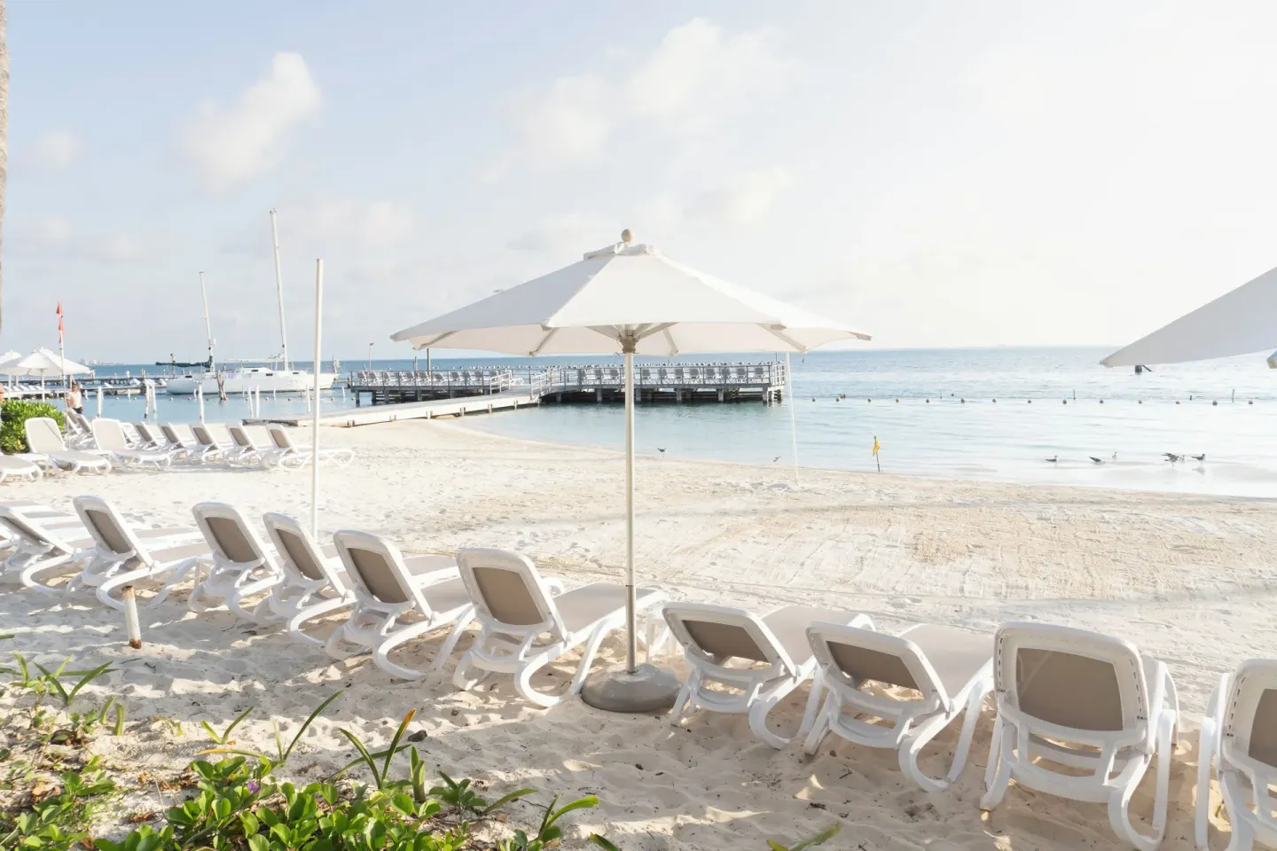 White lounge chairs and umbrellas on the beach by a pier at Cancun Bay Hotel.
