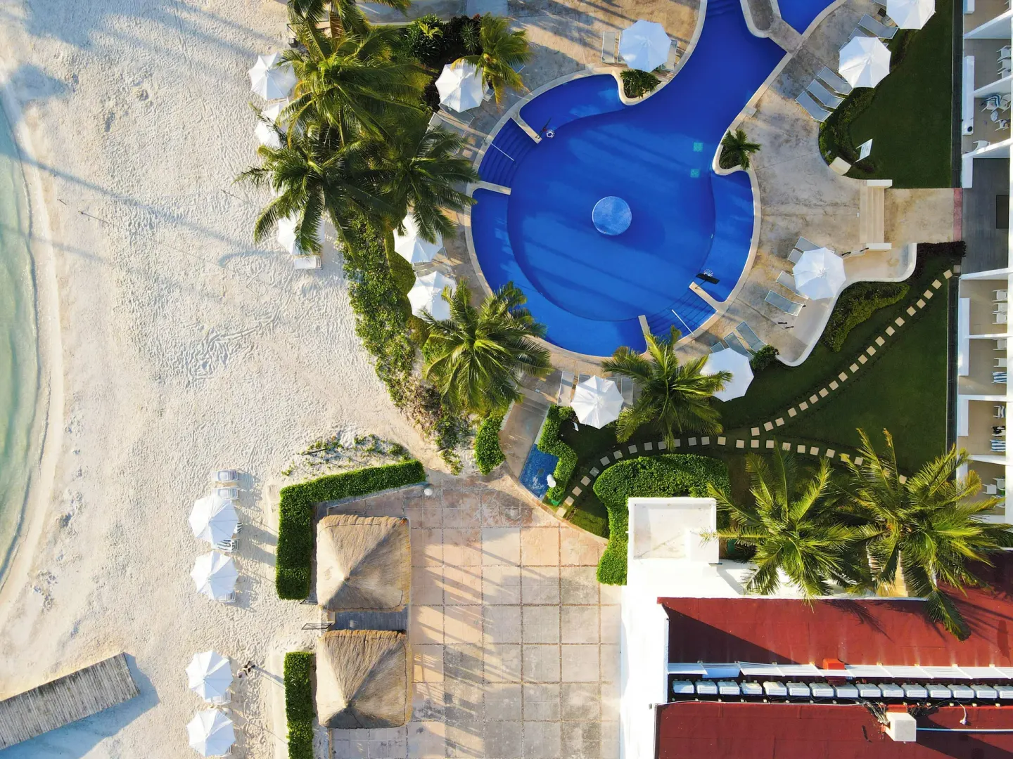 Aerial view of the beachfront pool, palms, umbrellas, and sand at Cancun Bay Hotel.
