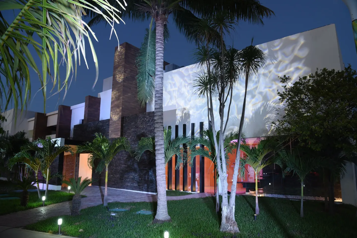 Nighttime exterior with palm trees, lawn, and illuminated building facade at Cancun Bay Hotel.