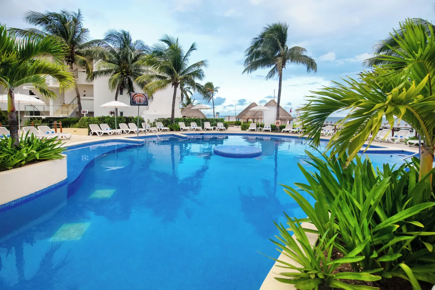 Pool with palm trees, loungers, and beach beyond at Cancun Bay Hotel.
