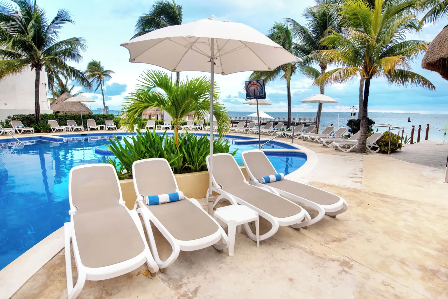 Poolside loungers under a white umbrella by the beach at Cancun Bay Hotel.