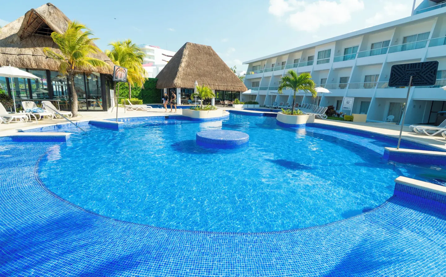 Bright blue resort pool with thatched buildings and guest rooms at Cancun Bay Hotel.