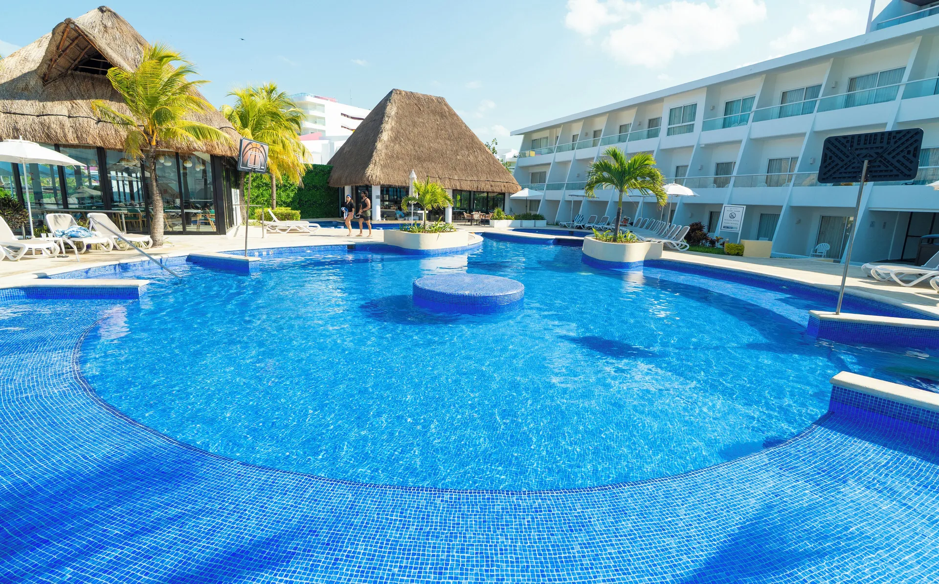 Bright blue resort pool with thatched buildings and guest rooms at Cancun Bay Hotel.