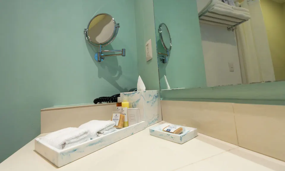 Standard Room bathroom counter at Cancun Bay Hotel with towels, toiletries, tissue box and mirror.