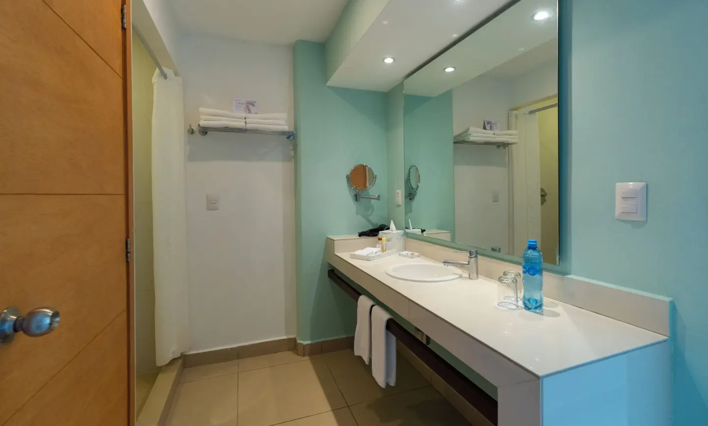 Standard Room bathroom at Cancun Bay Hotel with long vanity, mirror, towels and shower area.
