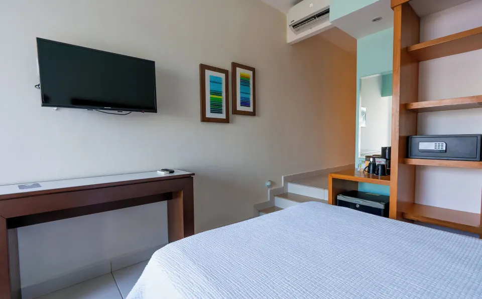 Standard Room at Cancun Bay Hotel with a bed, wall-mounted TV, desk, open shelving, safe and stairs.