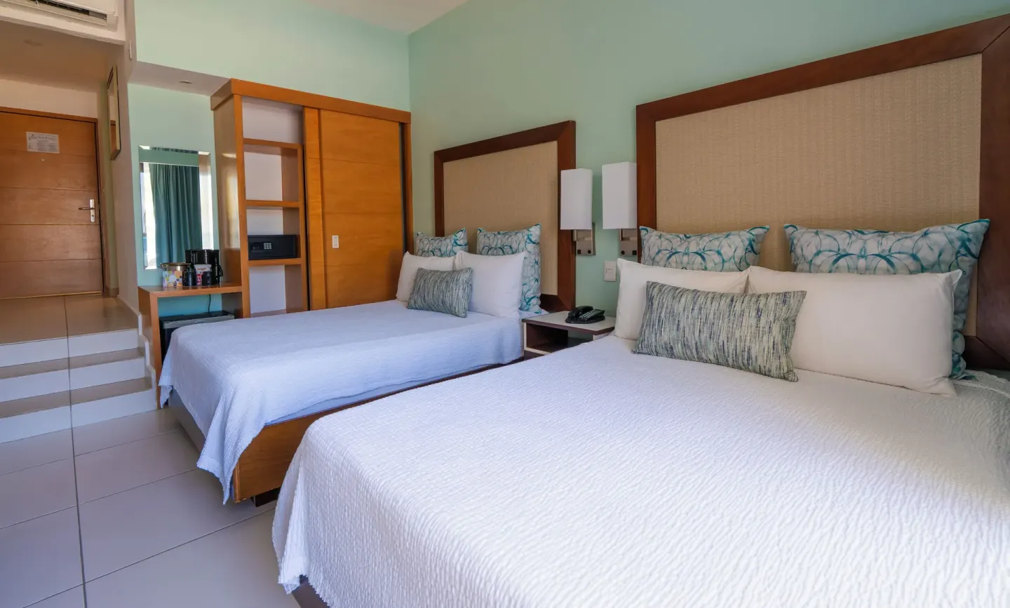 Standard Room at Cancun Bay Hotel with two beds, bedside table, wardrobe, safe and entry steps.