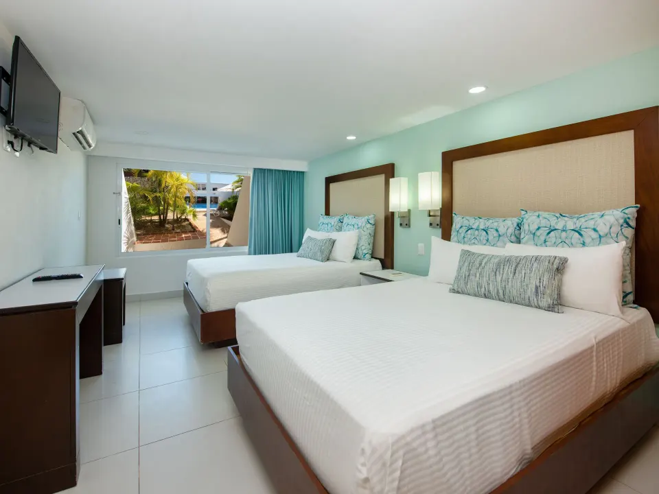 Standard Room at Cancun Bay Hotel with two beds, TV, desk and a window facing palms outside.
