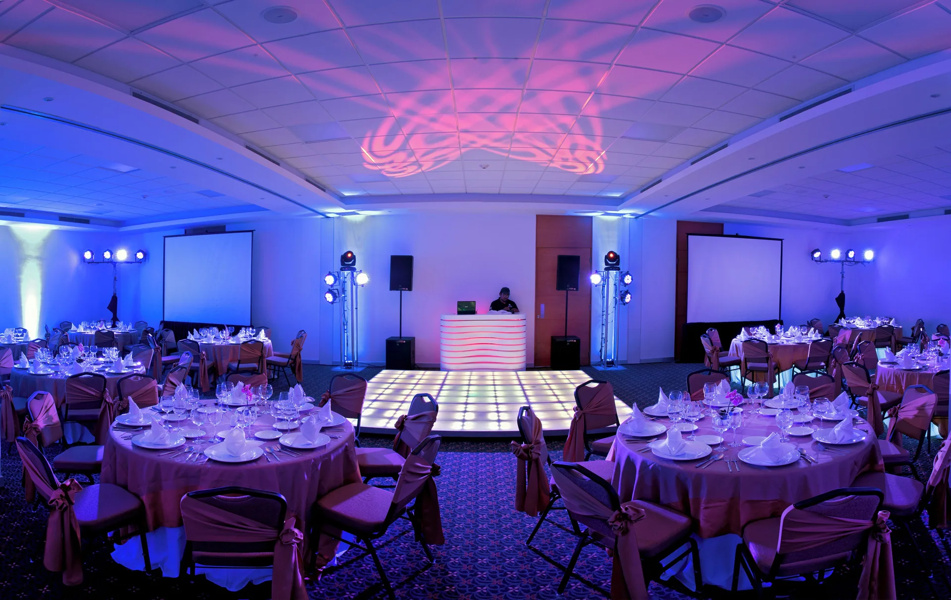 Banquet hall set with round tables, DJ booth, screens, and blue lighting at Cancun Bay Hotel.