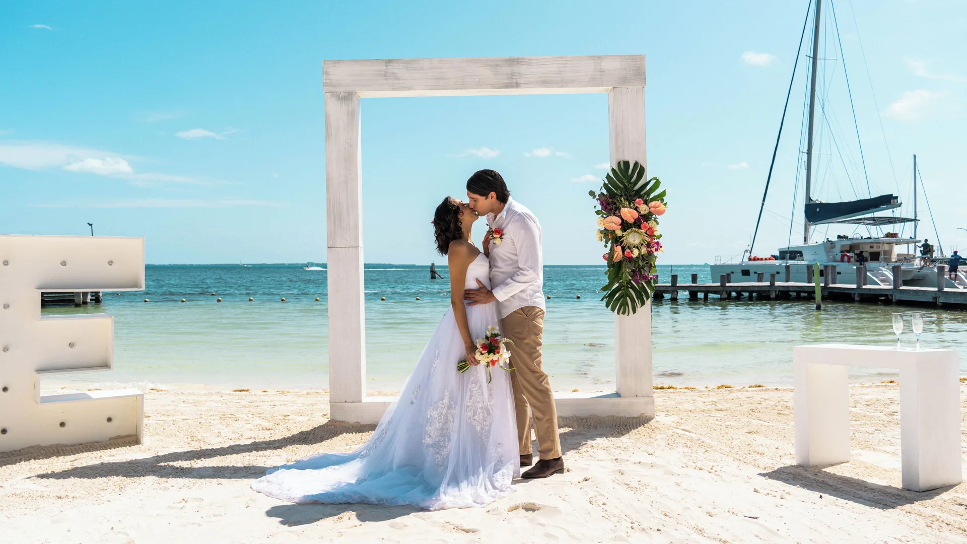 Beach wedding couple beneath a white frame by the water at Cancun Bay Hotel.
