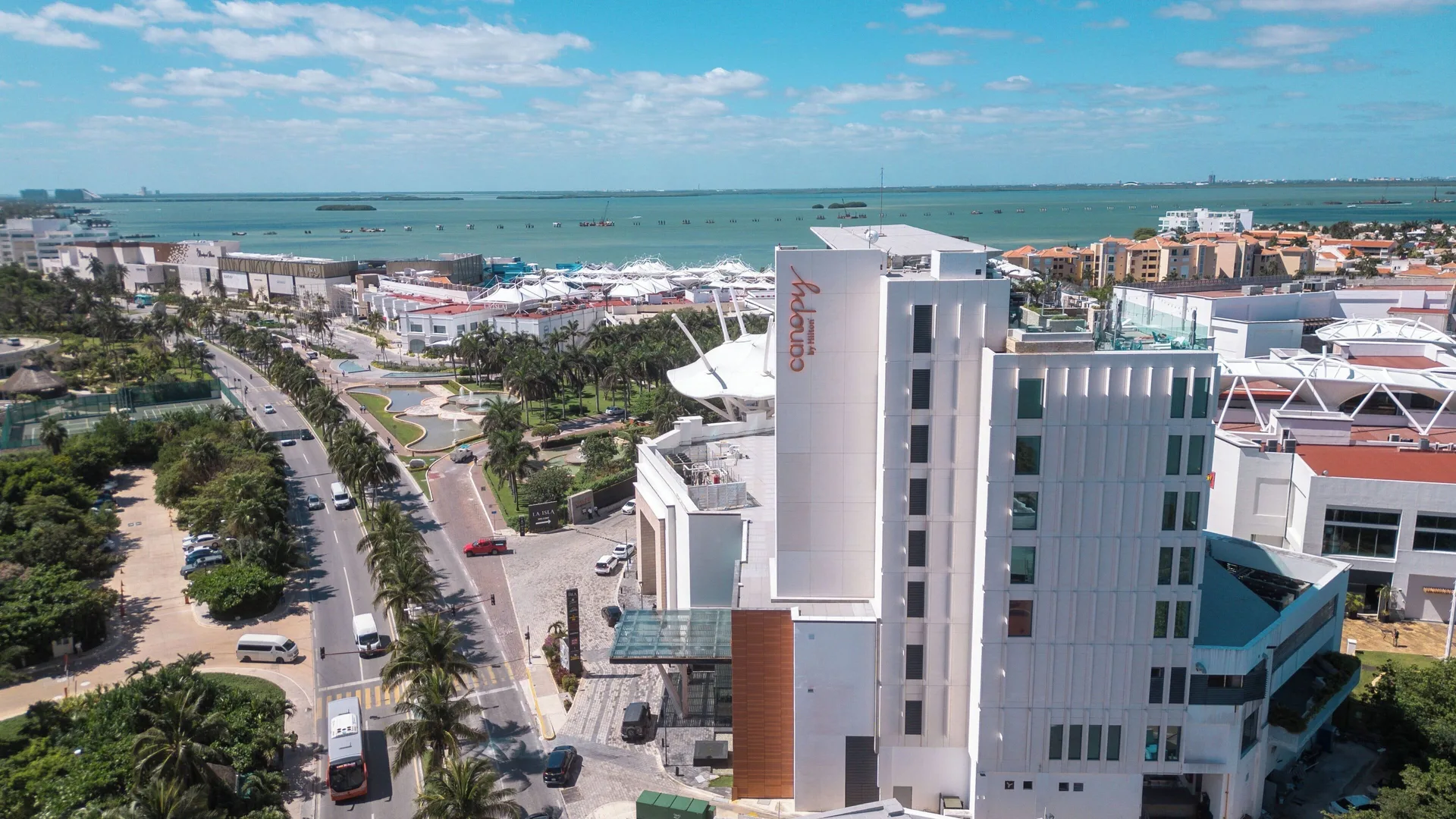 Aerial view of Canopy by Hilton Cancun La Isla beside the lagoon and palm-lined road.