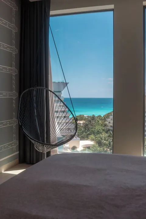 Hanging chair by a guest room window with ocean view at Canopy by Hilton Cancun La Isla.